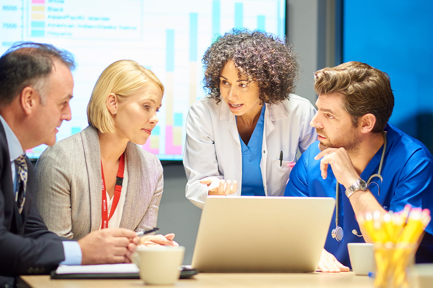 A group of doctors and business people gathered around a laptop and talking.