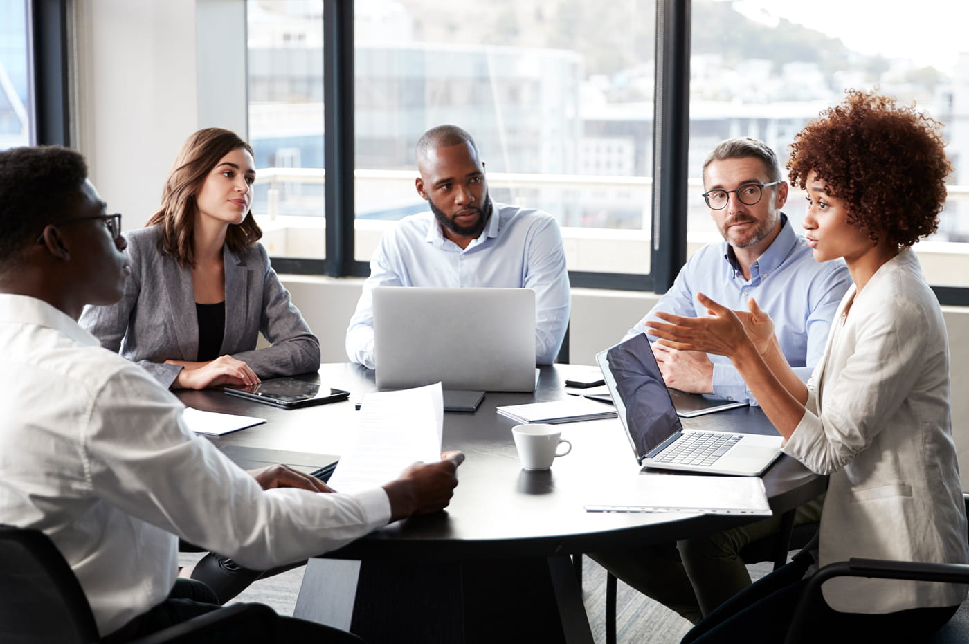 A group of business people gathered around a table with one woman talking.