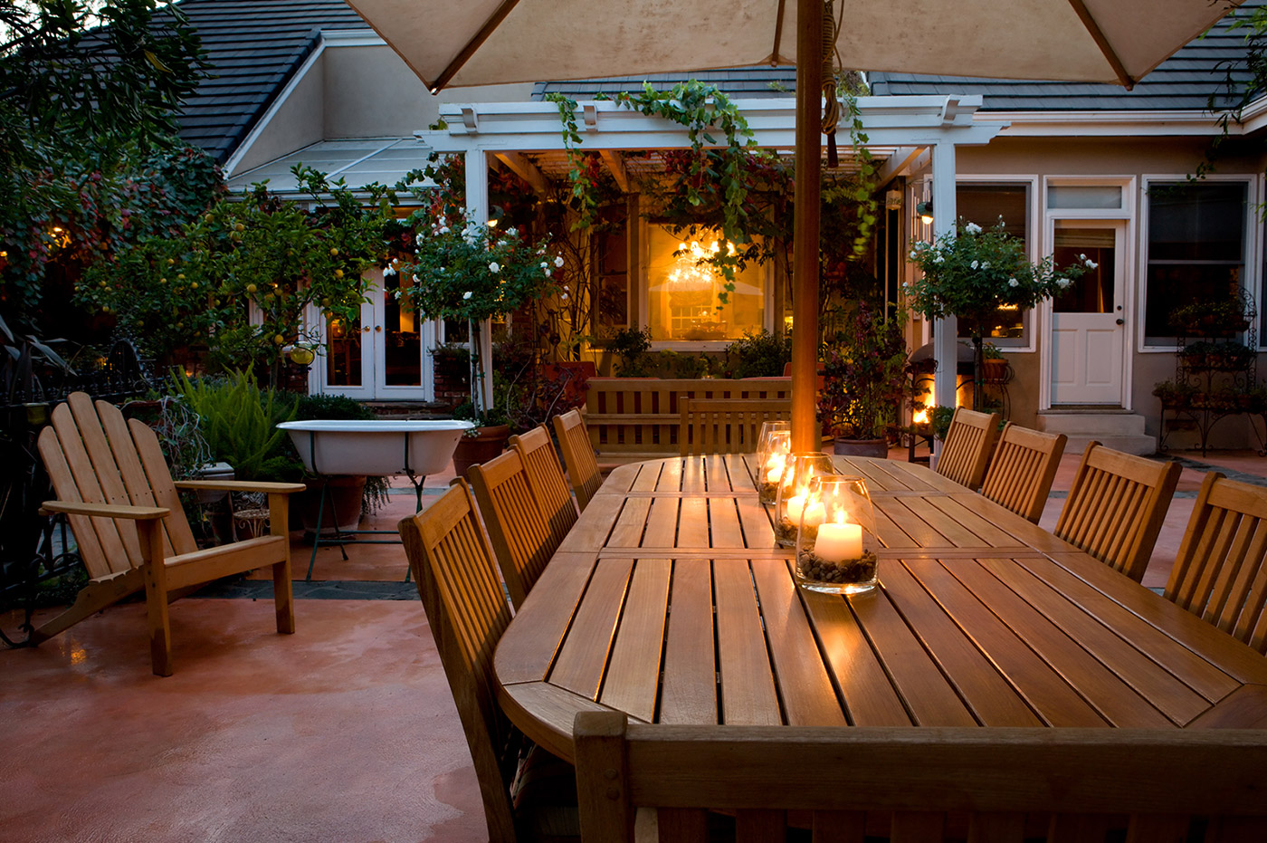 An outdoor patio with a large, wooden dining table under an umbrella.