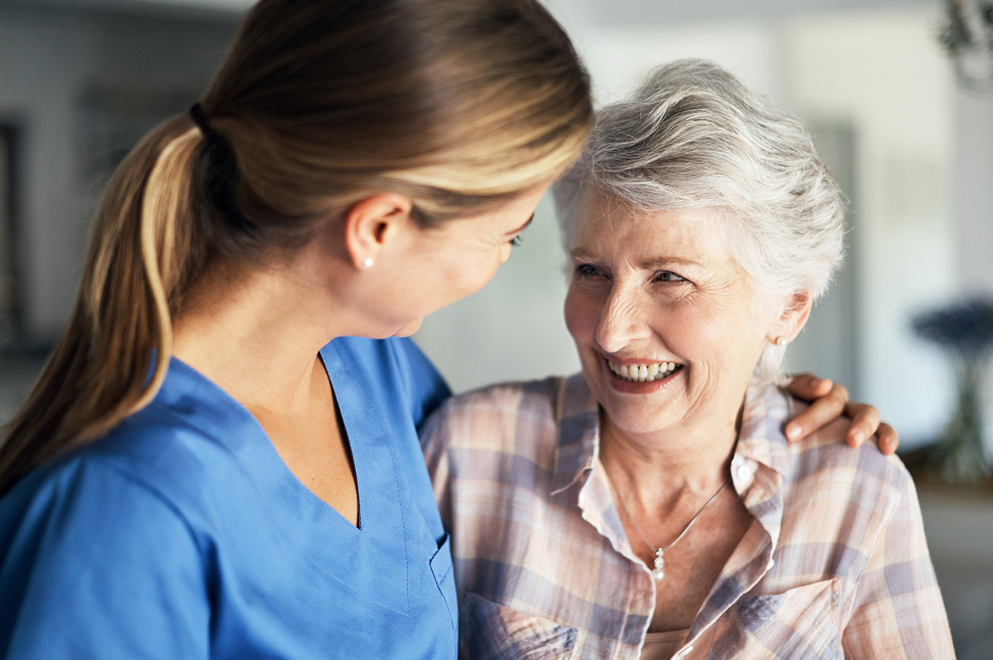 A healthcare worker with her arm around an older patient's shoulder, they are smiling.