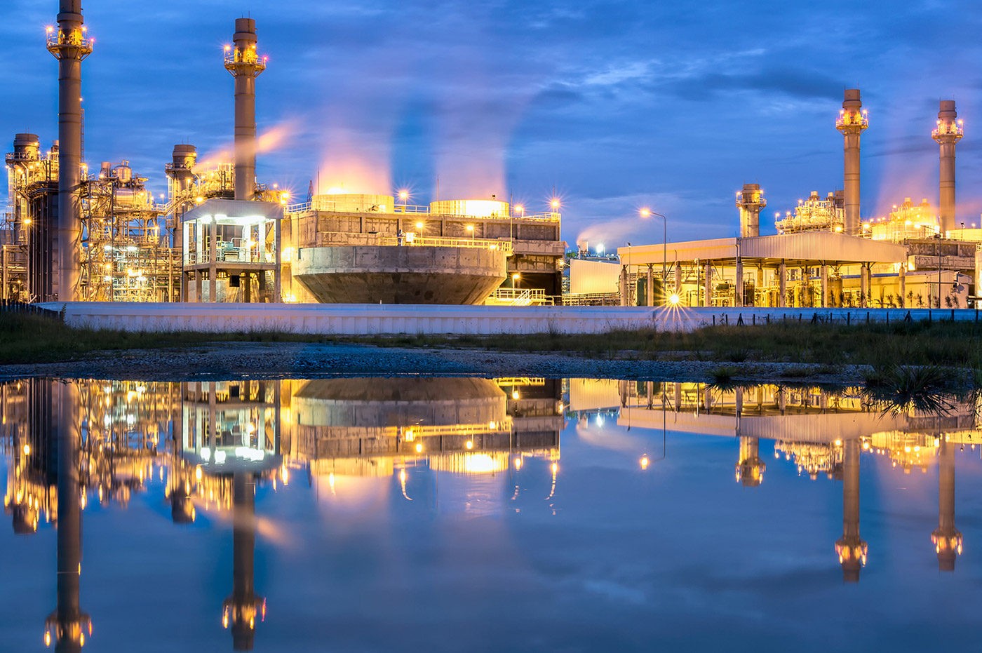 A large powerplant situated next to a body of water, with the reflection of the powerplant.