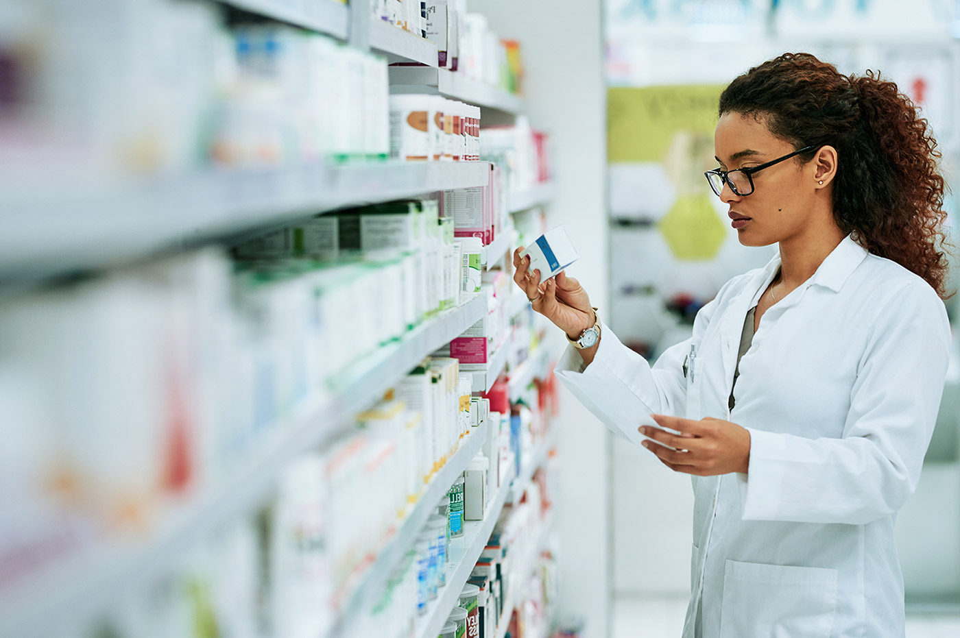 A healthcare worker looking at a box of medicine in a pharmacy.