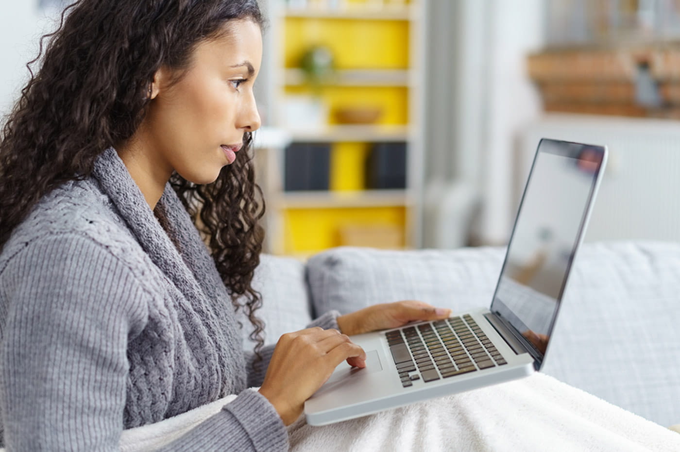 A woman working on her laptop on the couch.