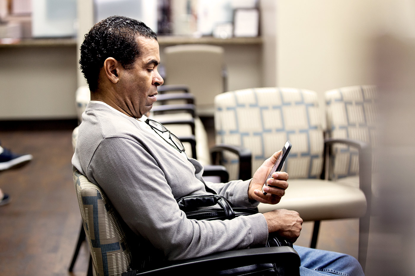 A man in a doctor's office waiting room looking at his cell phone.