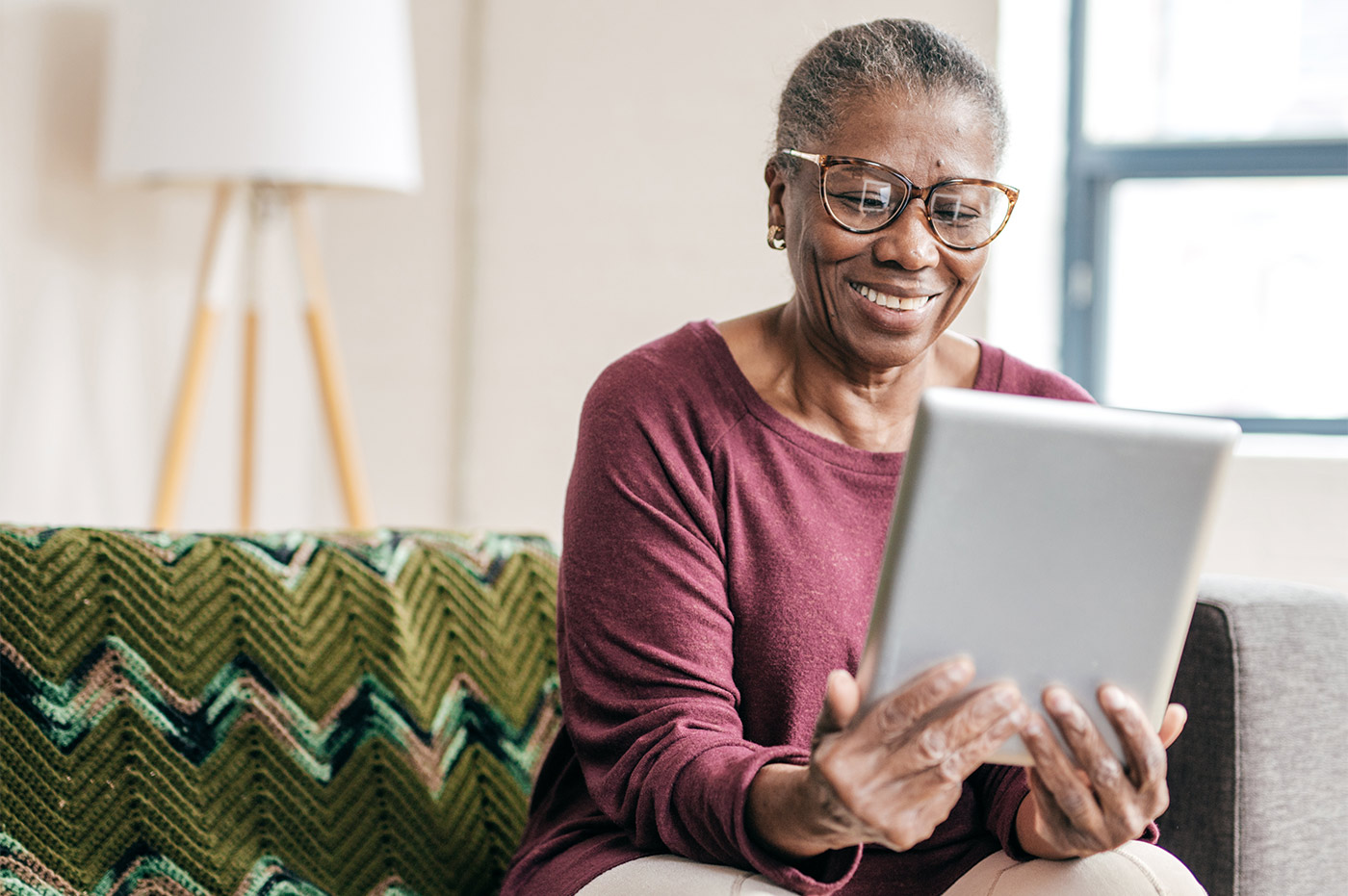 An older woman smiling at something she is looking at on an iPad.