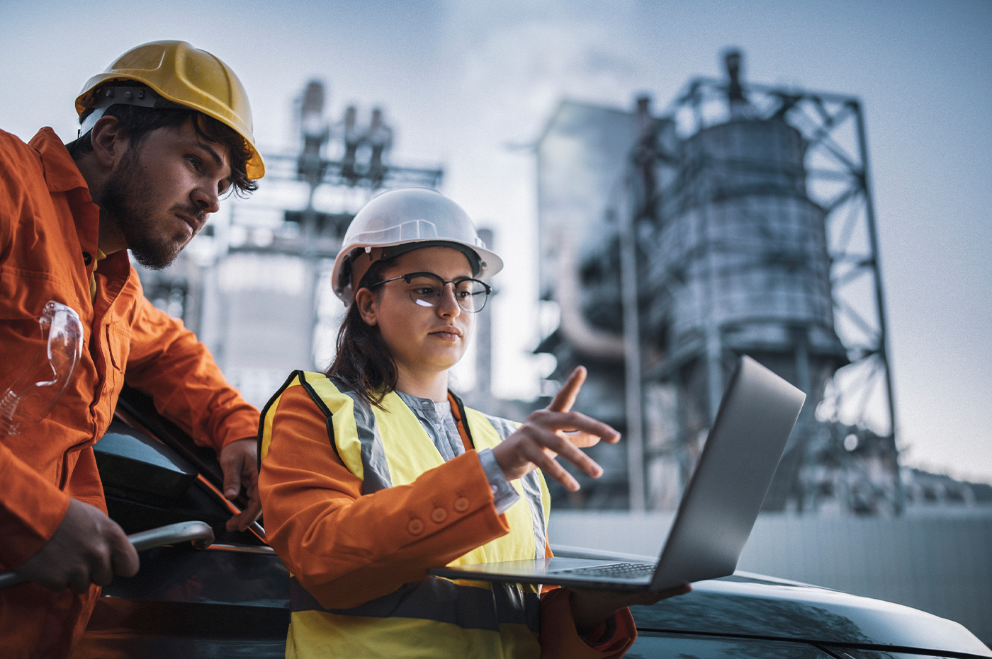 Man and woman workers in hard hats looking at a laptop on a power grid site