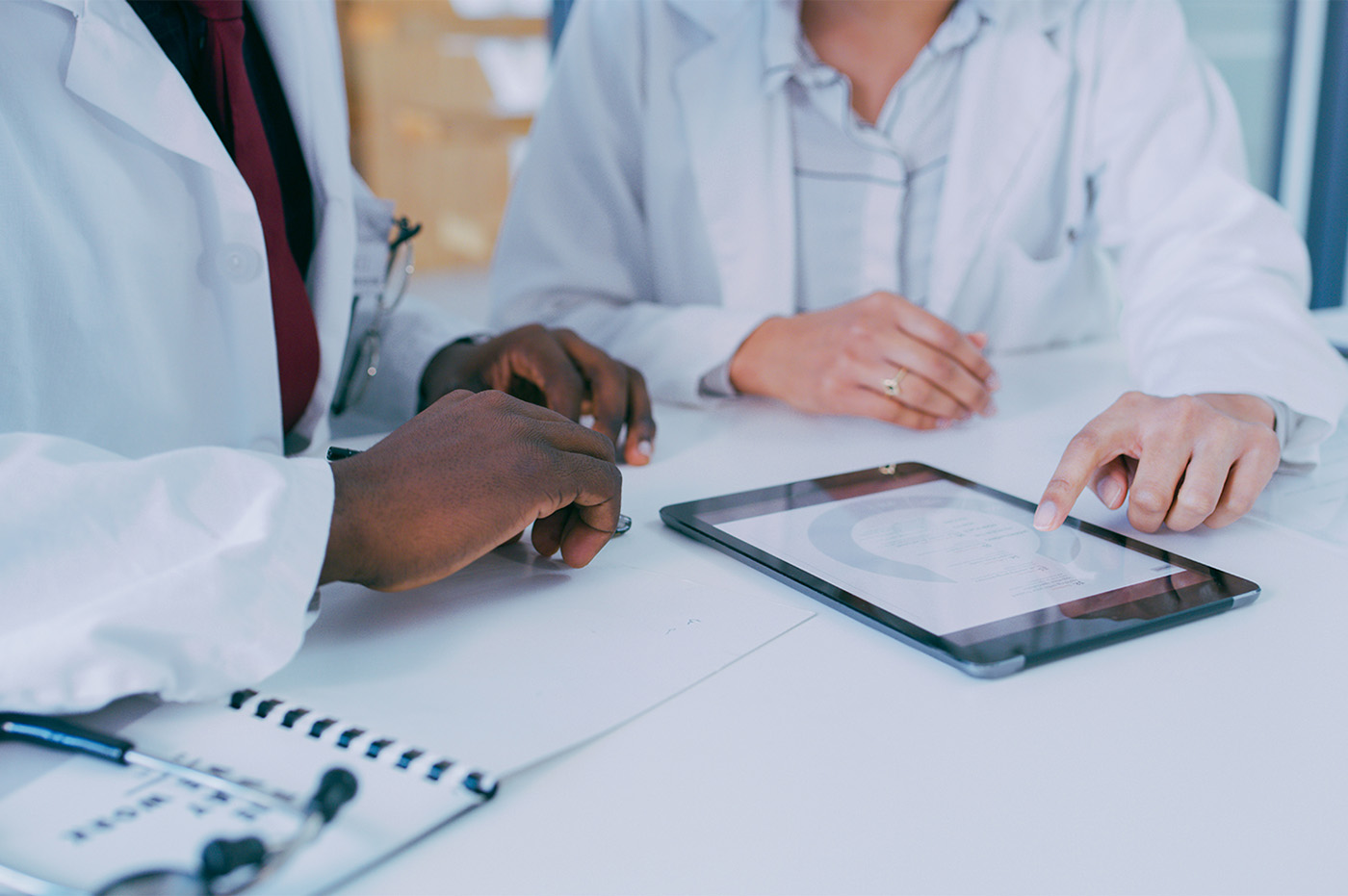 Two healthcare workers in lab coats working on a tablet together.