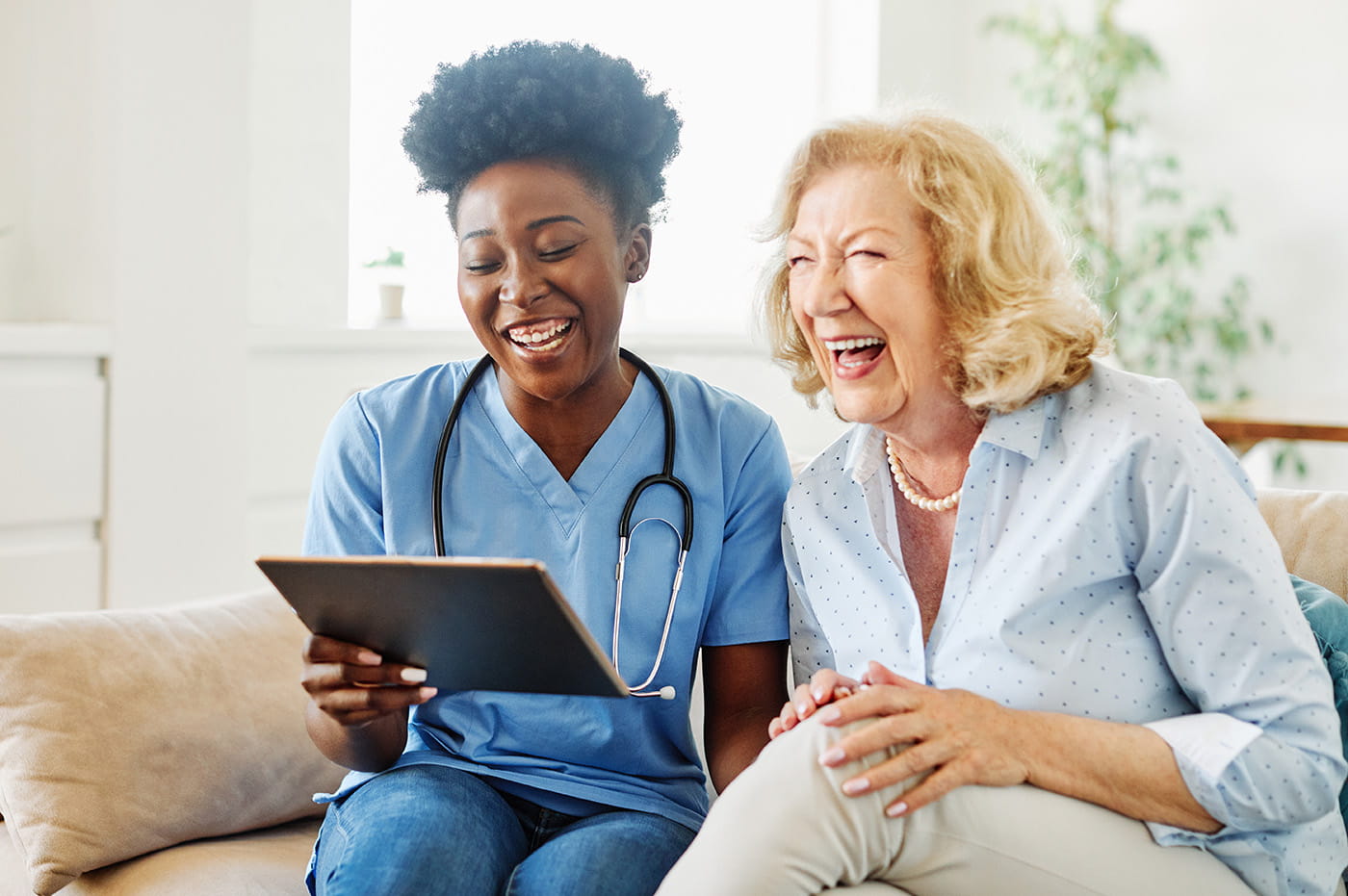 An older woman and female healthcare worker sitting together and laughing.