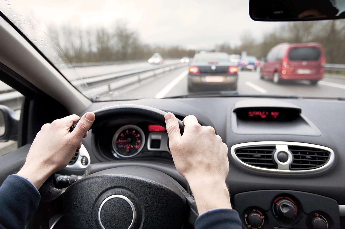 A pair of hands holding a car steering wheel and driving.