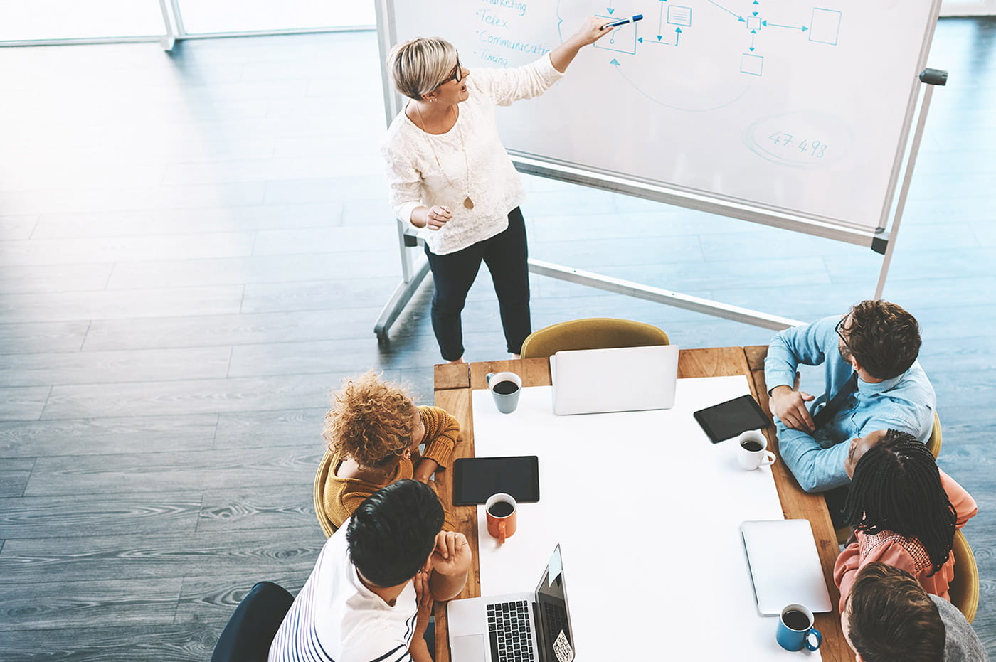 A group of professionals seated around a table listening to a woman presenting.