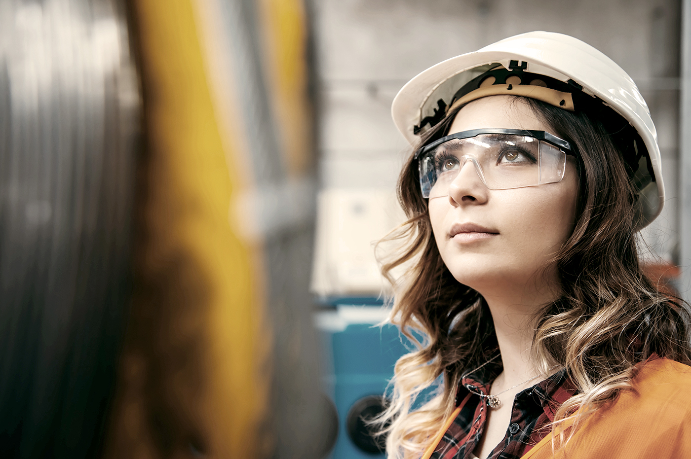 A woman wearing safety goggles and a hardhat working.