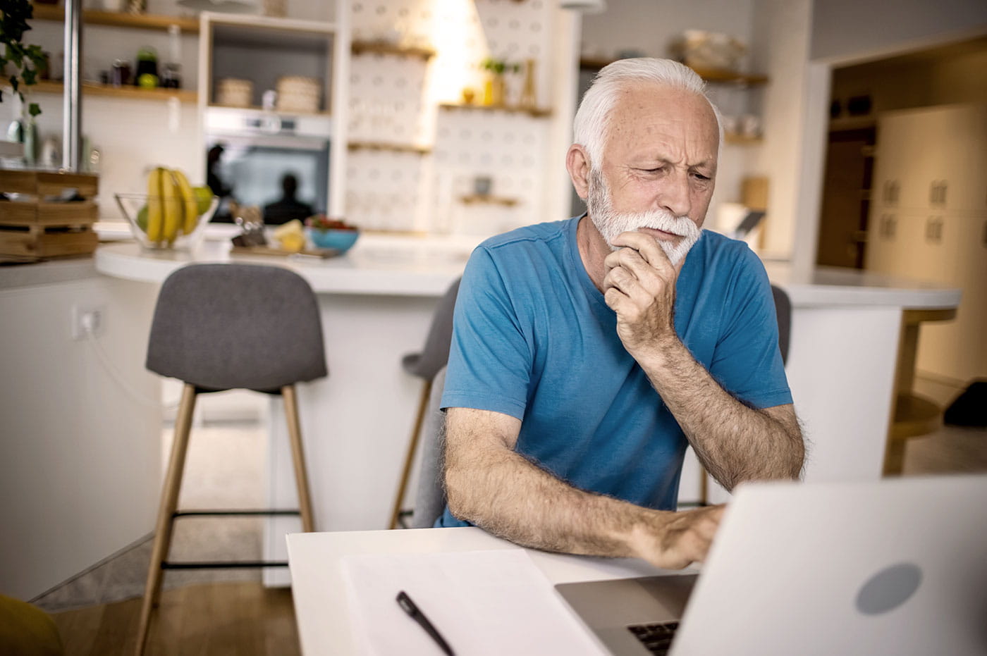 An older man working on his laptop at home.