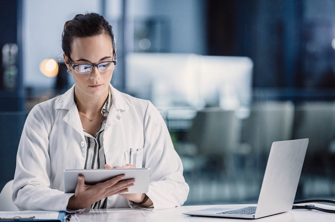 A female doctor working on a tablet and a laptop computer.