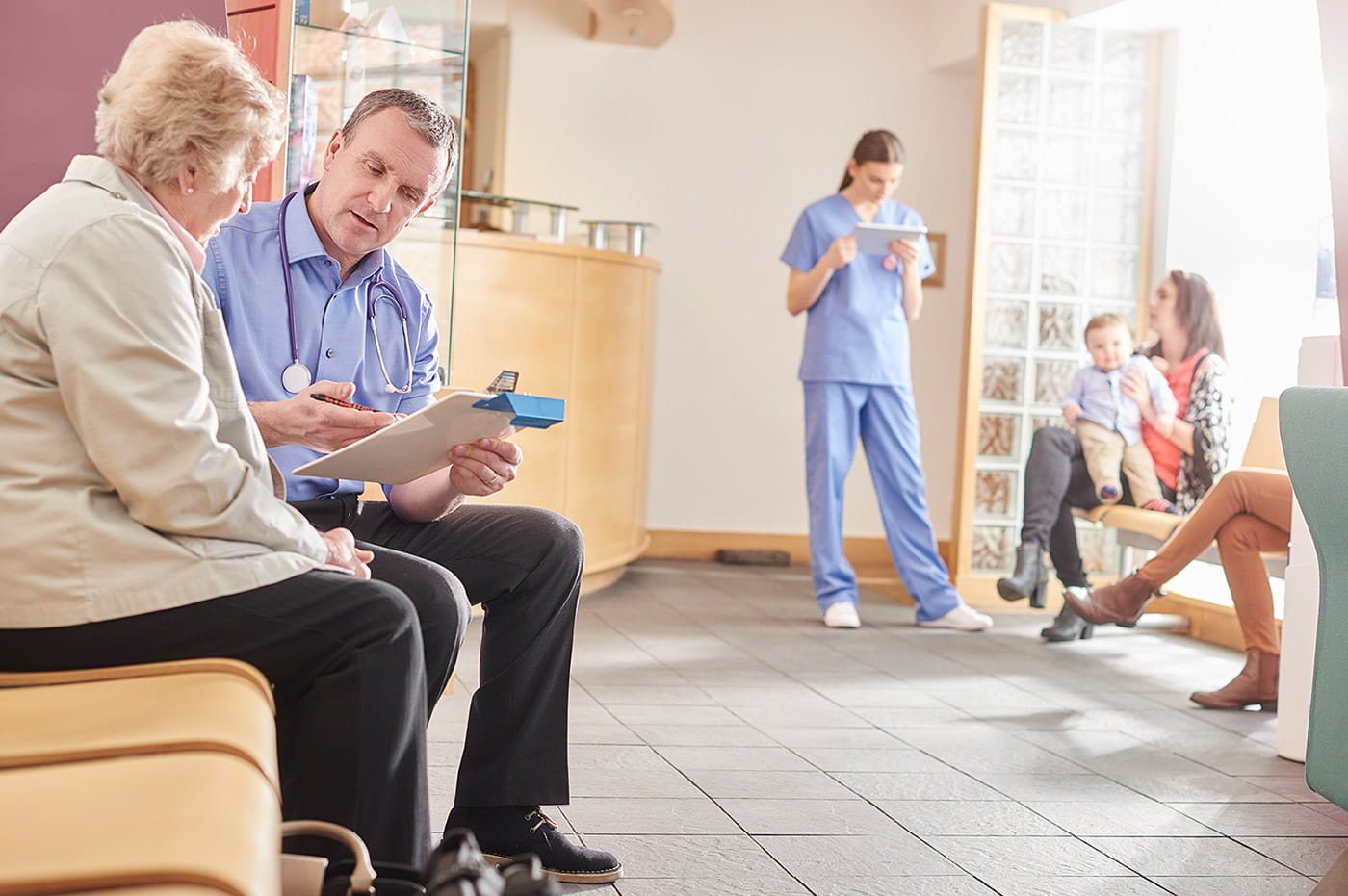 Multiple healthcare workers in a medical waiting room talking to their patients.