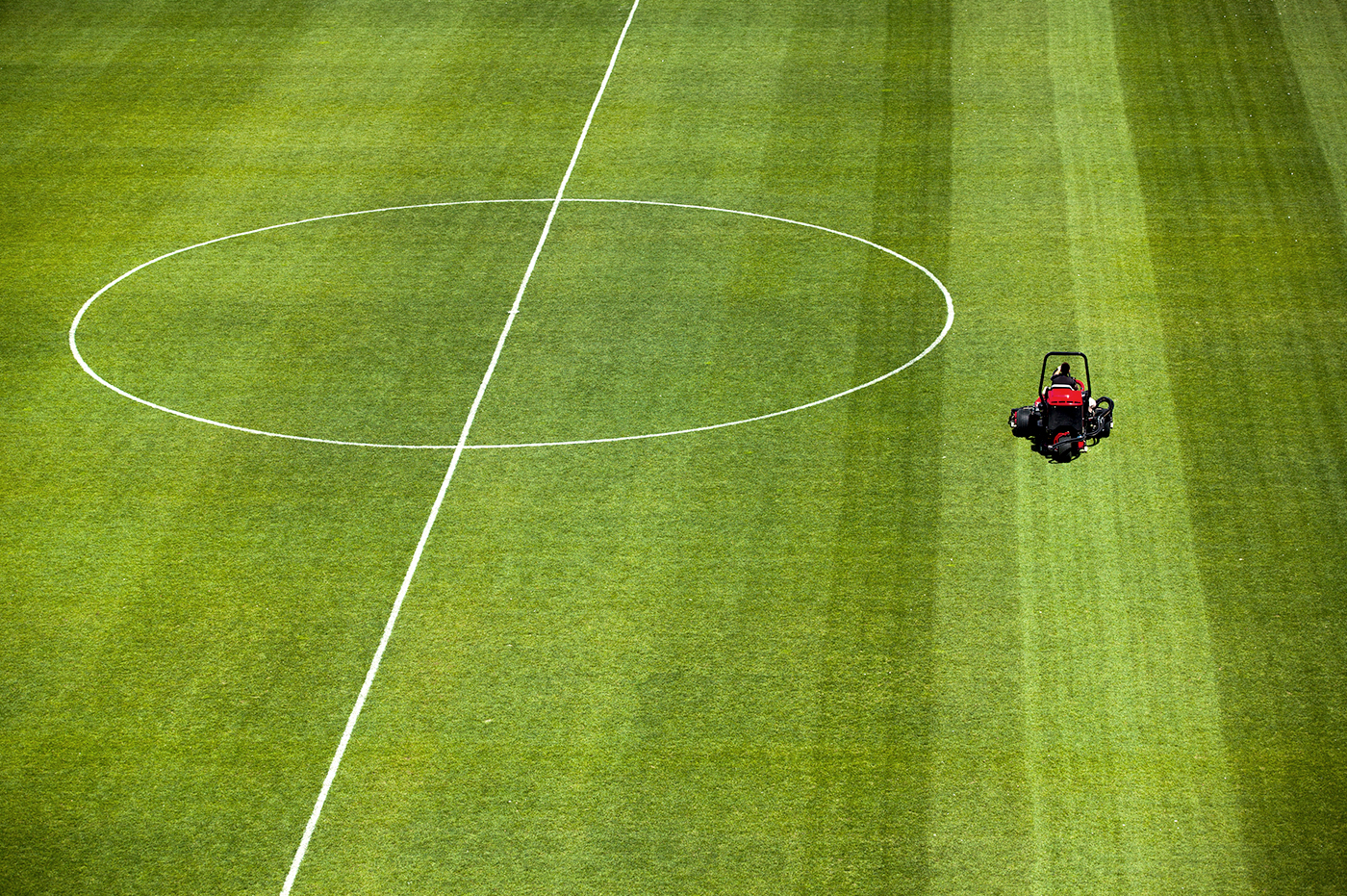 A person using a riding lawn mower to cut the grass on a soccer field.