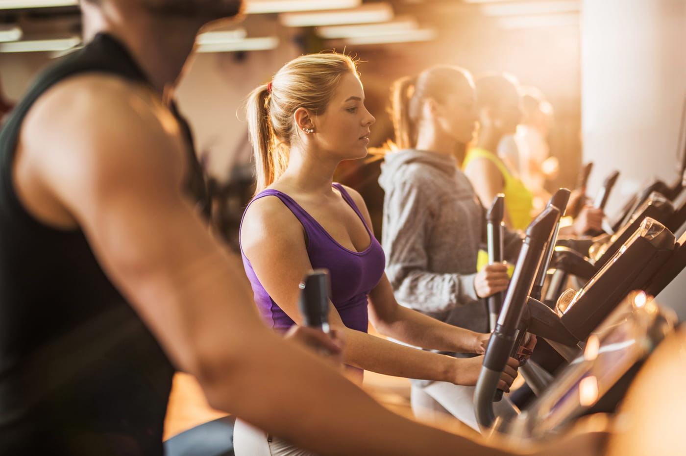 A row of people on elliptical fitness machines.