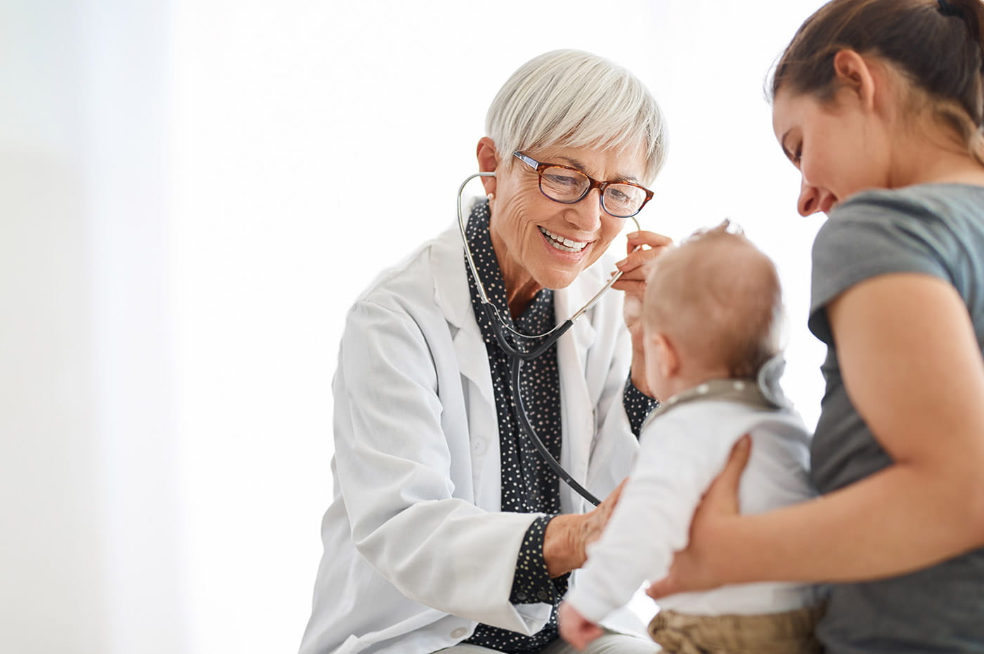 An older doctor listening to a baby's heartbeat using a stethoscope.