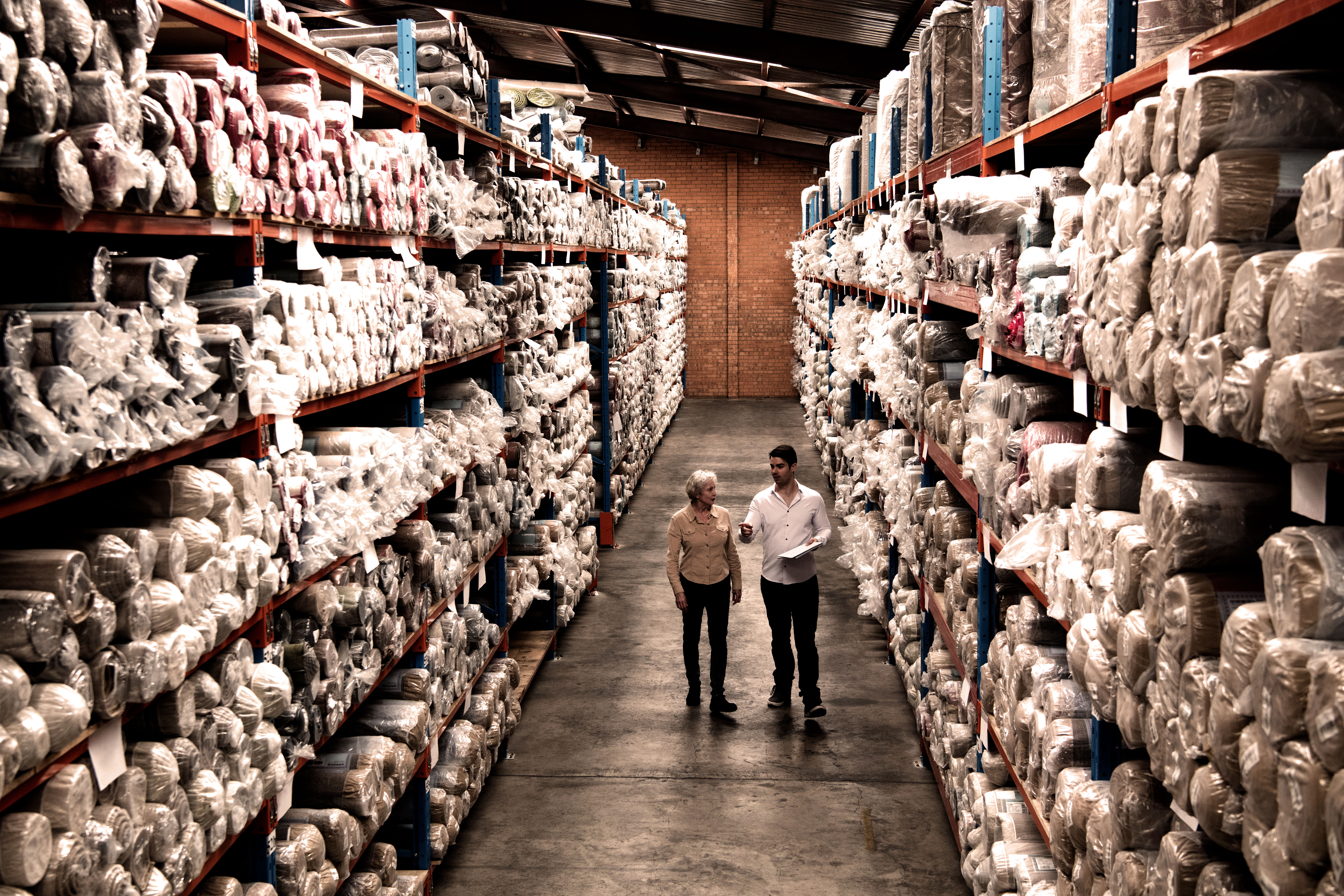 Two people in a rug warehouse.