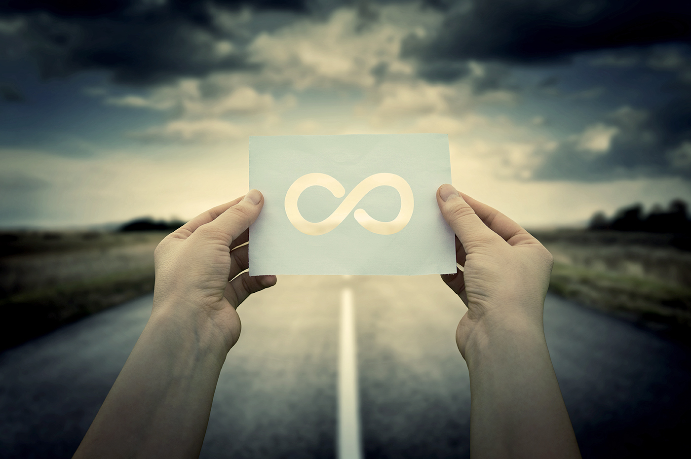 Hands holding an infinity-shaped cutout in front of a road.