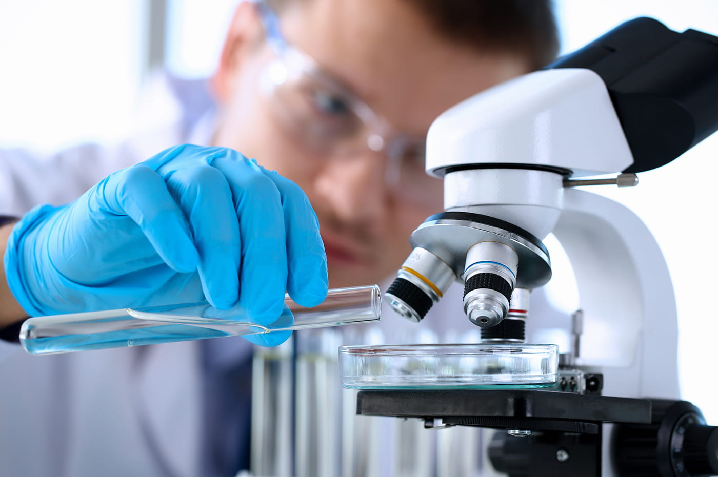 Man wearing lab coat and gloves pouring a substance into a microscope