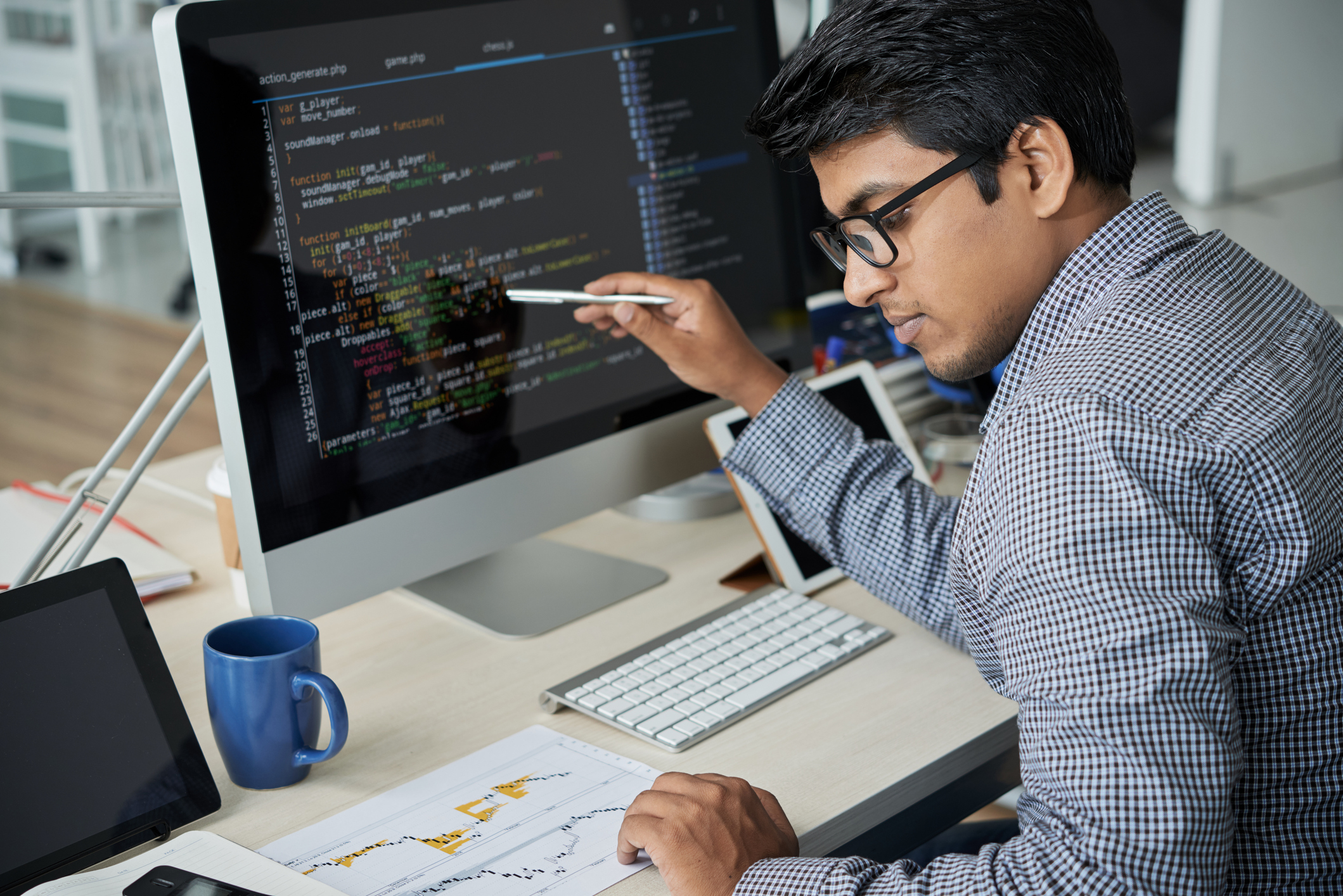 Man looking at data on a piece of paper while referencing code on a screen