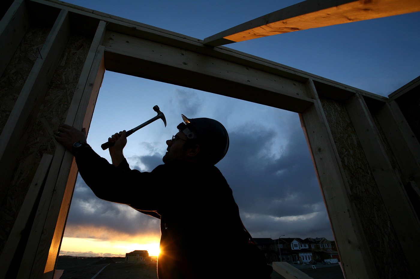 A silhouette of a construction worker building the frame of a house.