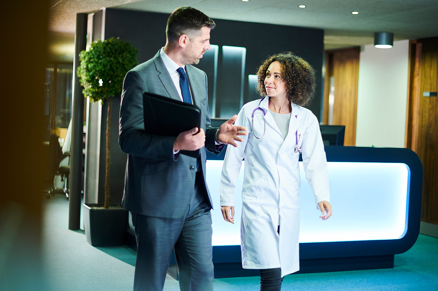 A female healthcare worker talking to a man in a suit.
