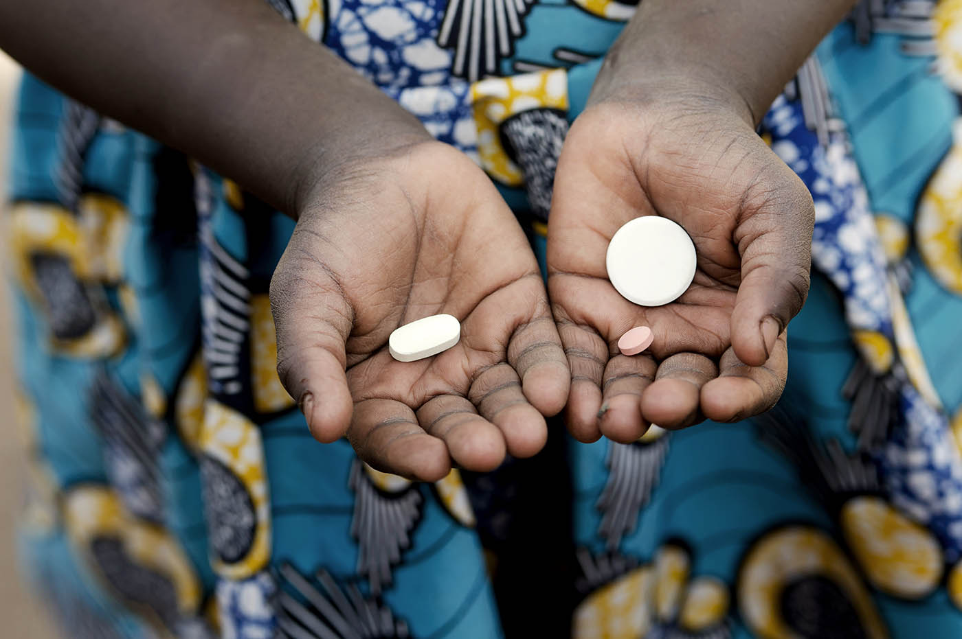 A pair of hands holding 3 tablets of medicine.