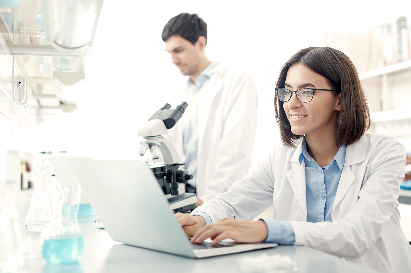 Two researchers working in a lab with a microscope and laptop.