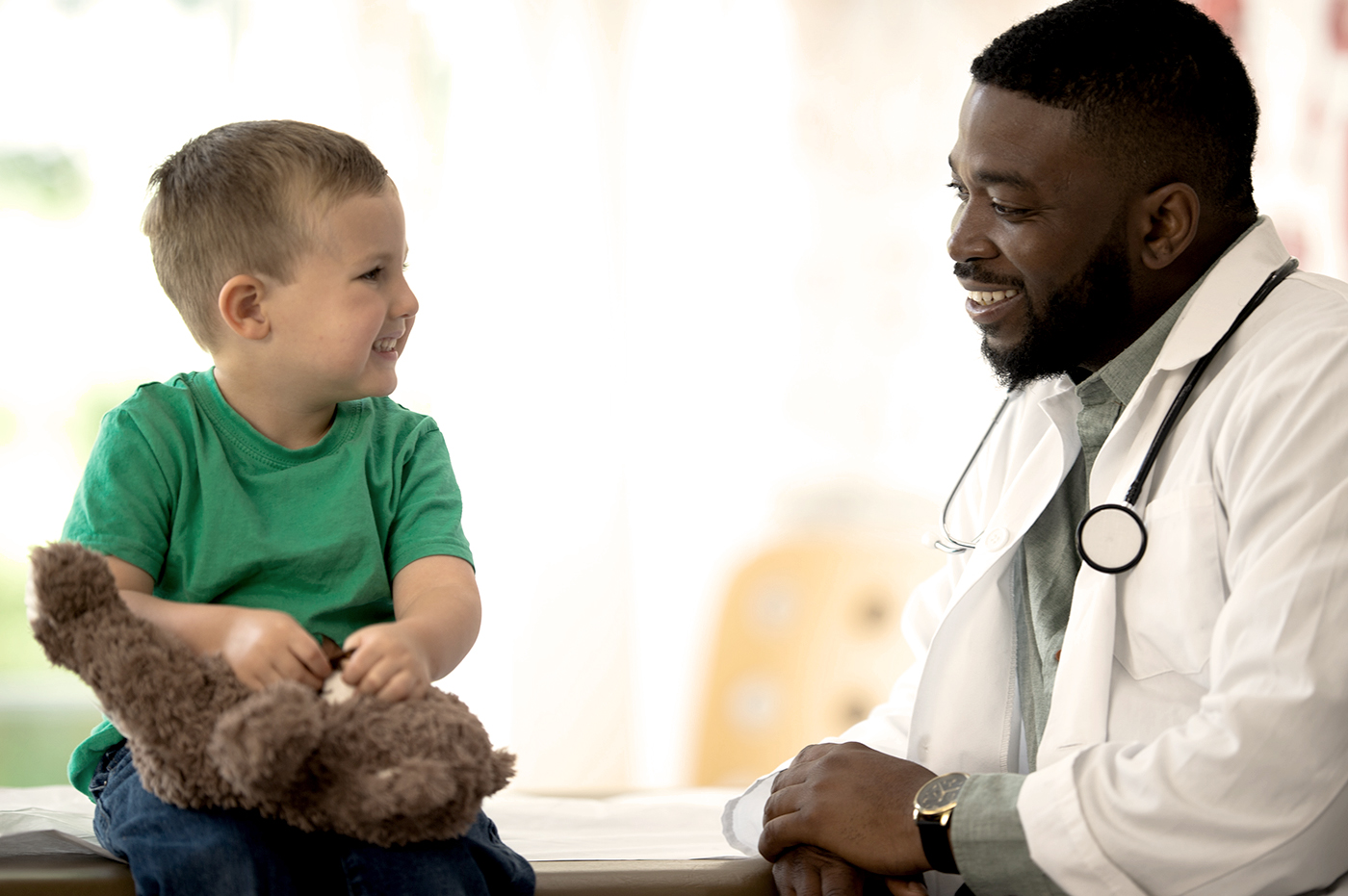 A little boy with a teddy bear with his doctor.