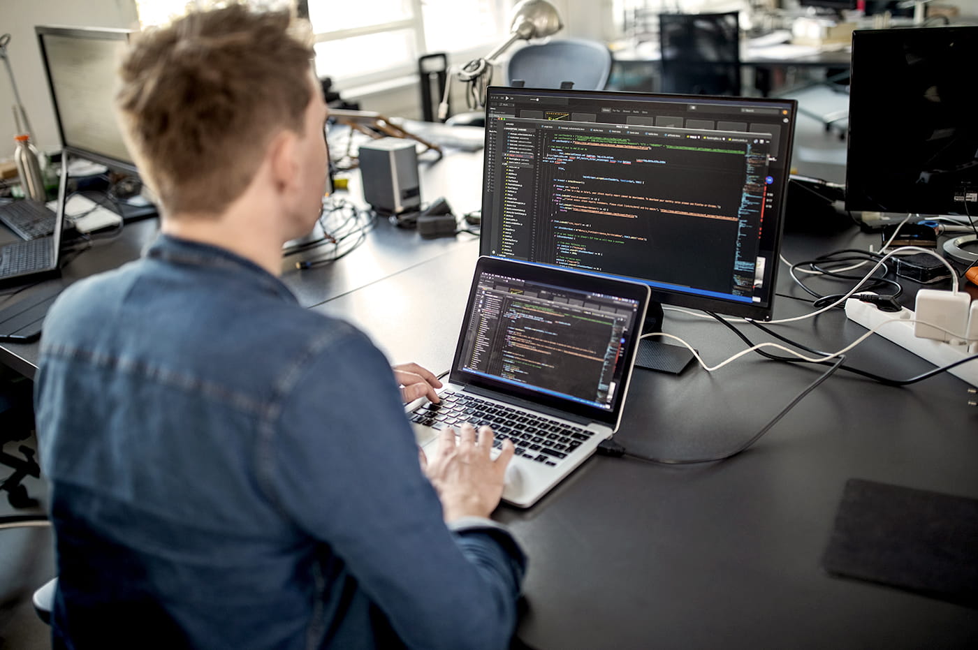 A man working on coding on a laptop and monitor.