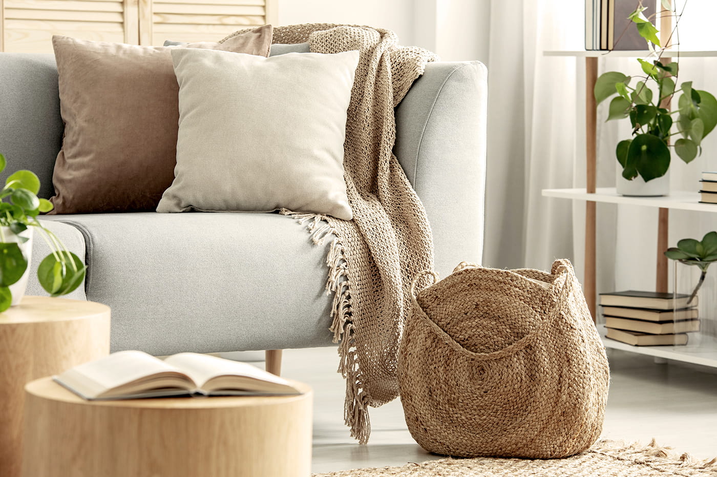 A grey sofa with a beige blanket and wicker basket next to it.