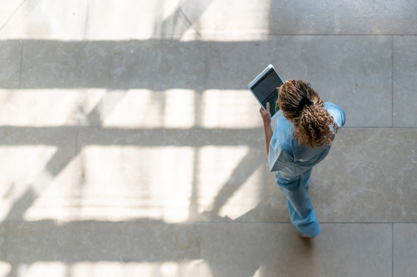 A female healthcare worker using a tablet and walking.