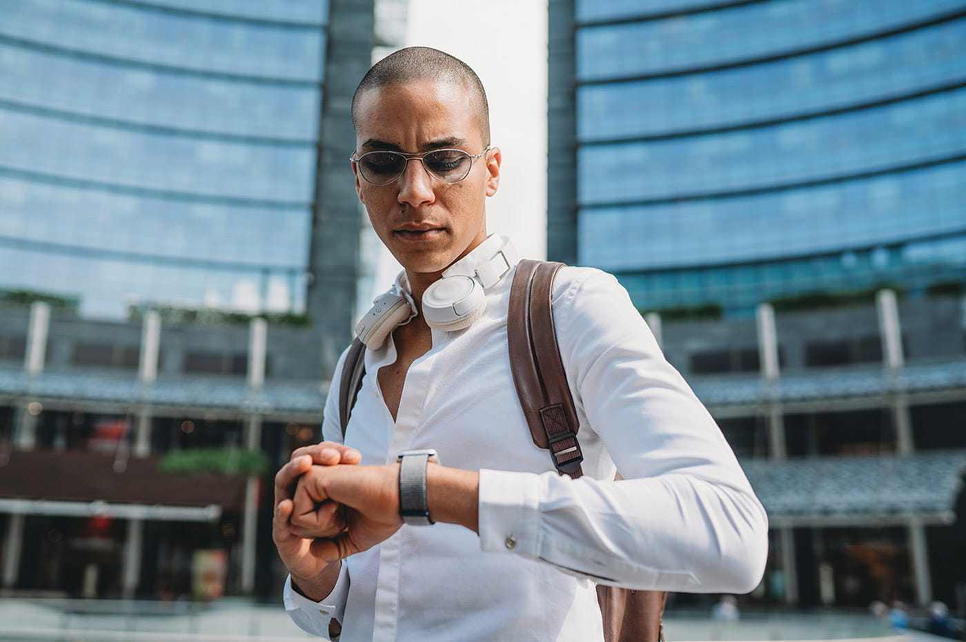 A man in glasses and with headphones looking at a smart watch.