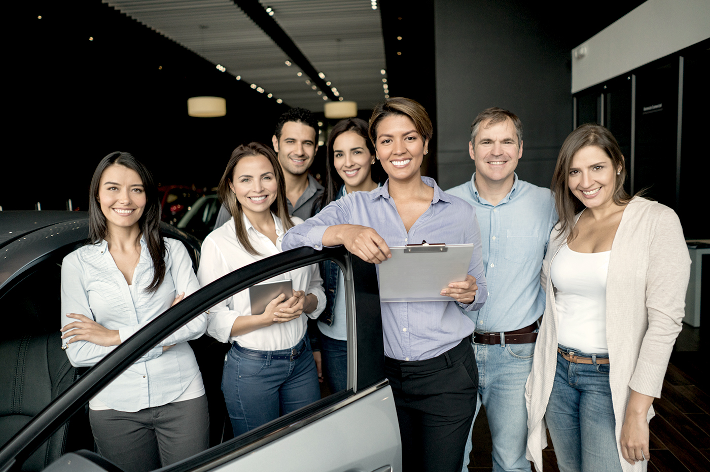 A group of people standing in front of a car door. 