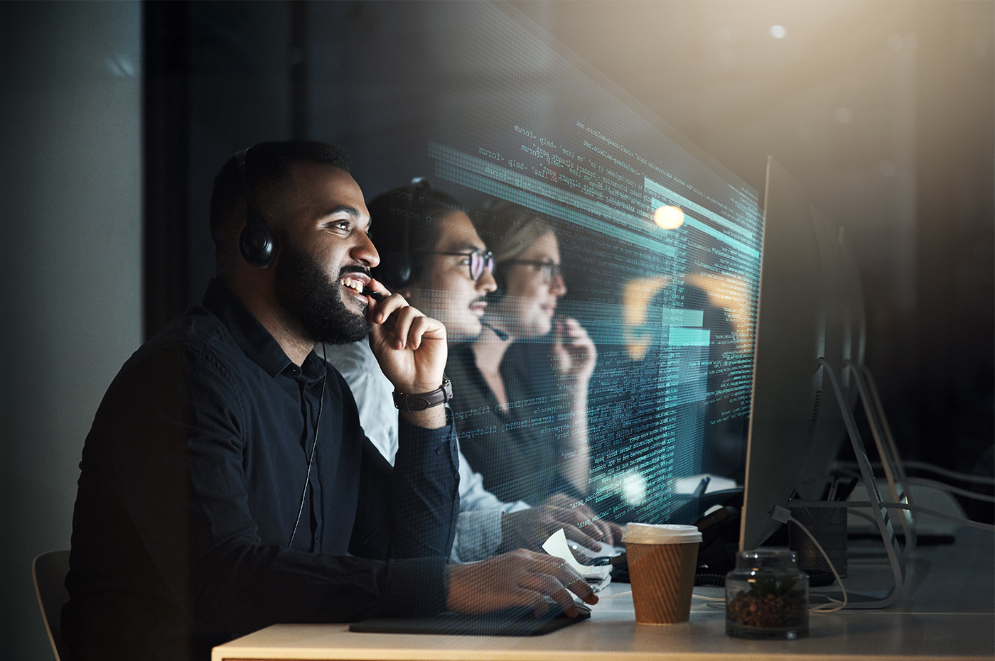 Three colleagues sitting next to each other looking at their computers and wearing headsets.