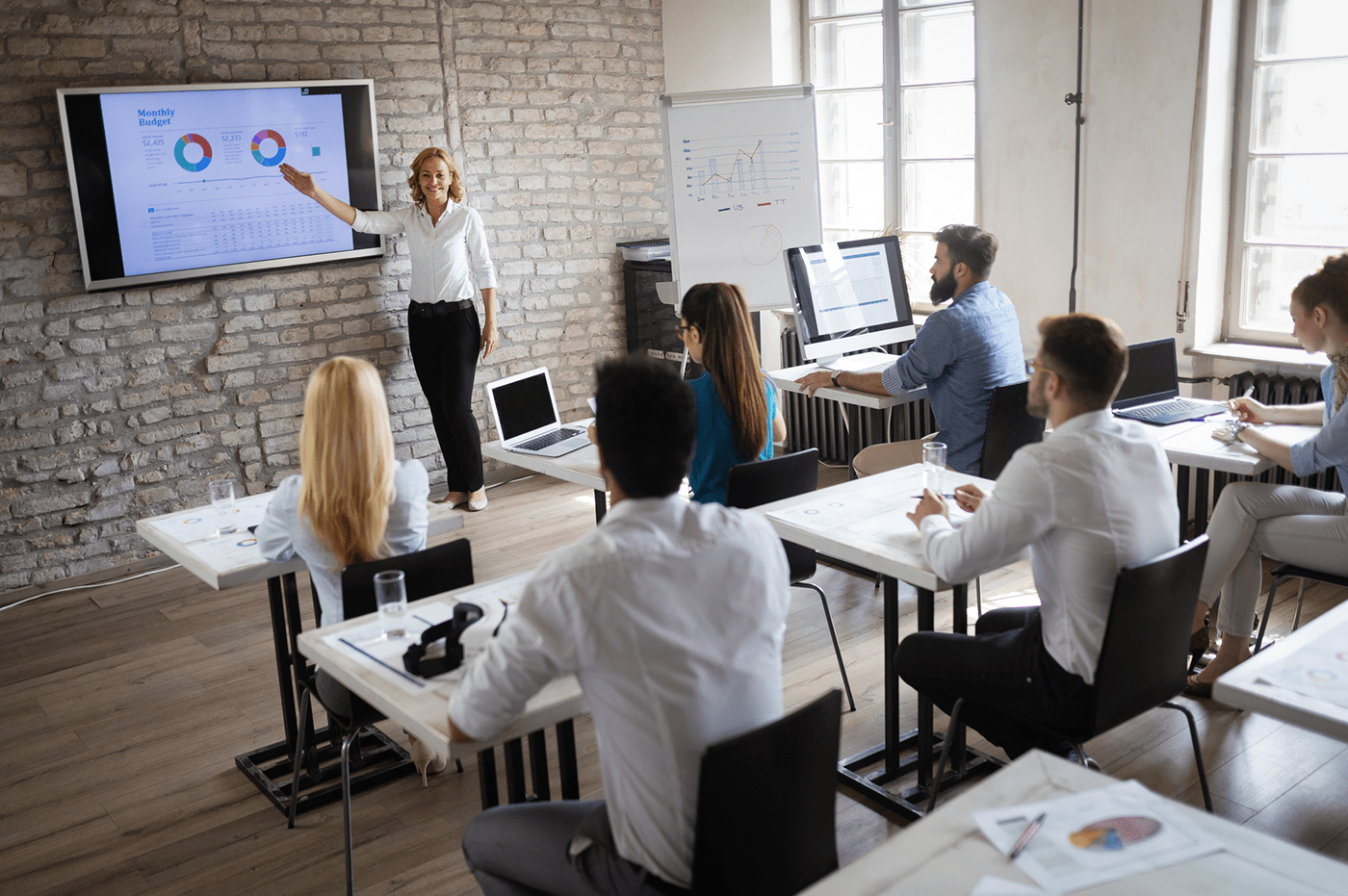 Women presenting data to a room of colleagues. 