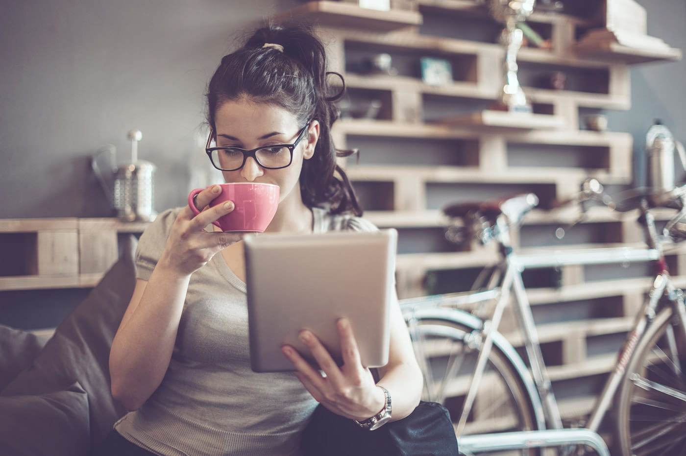 A woman sipping a warm beverage and looking at a tablet.