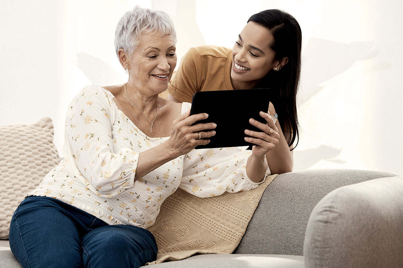 Young woman holding a tablet in front of a older woman smiling