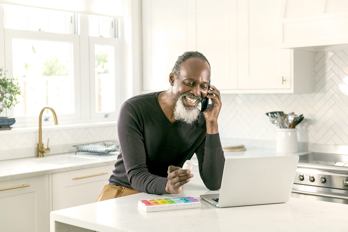 A man with a pill organizer talking on the phone and looking at a computer.