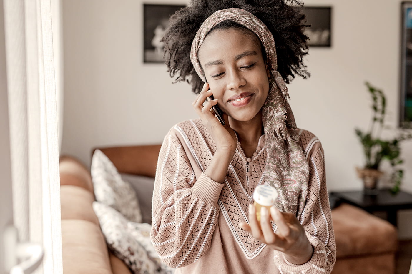 A woman talking on her cellphone and looking at a prescription medicine bottle.