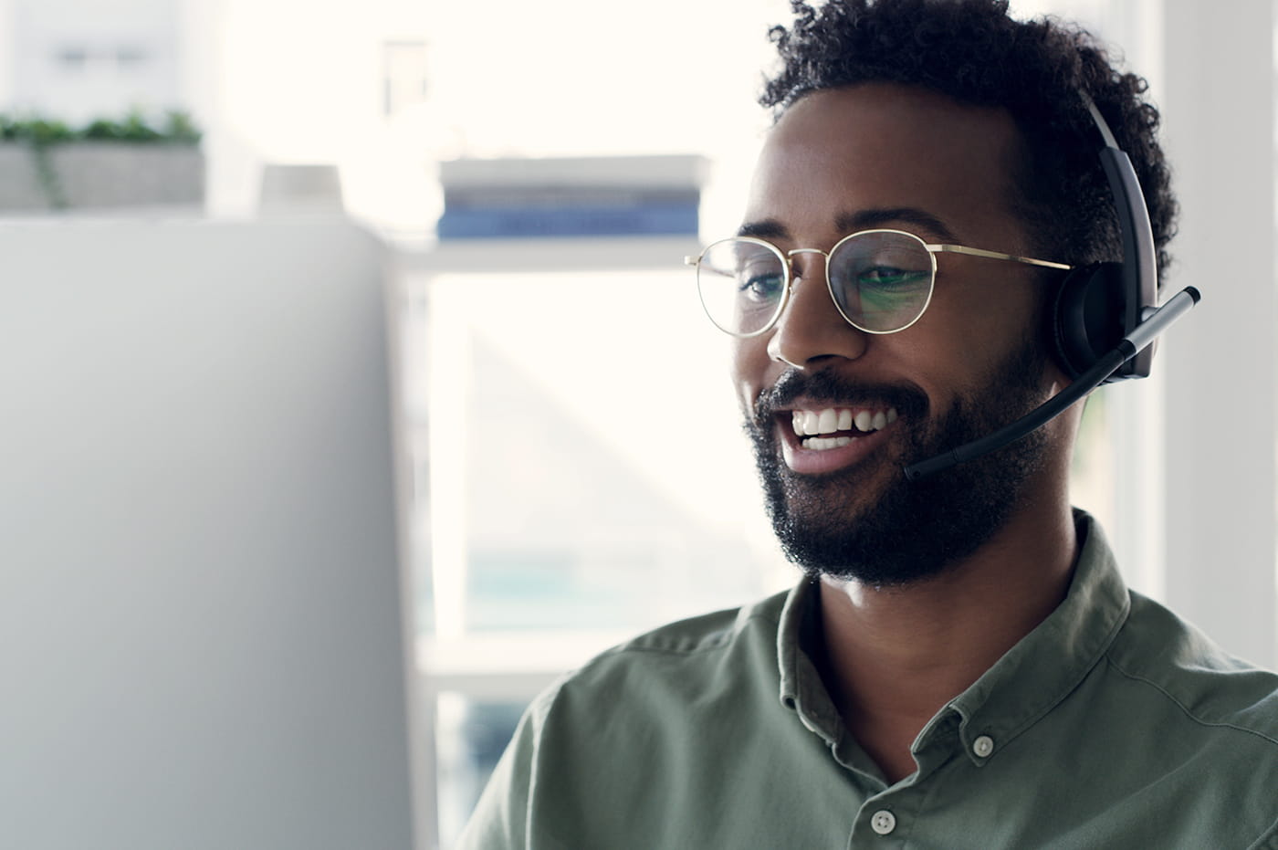 A young man seated at a computer talking on a headset.