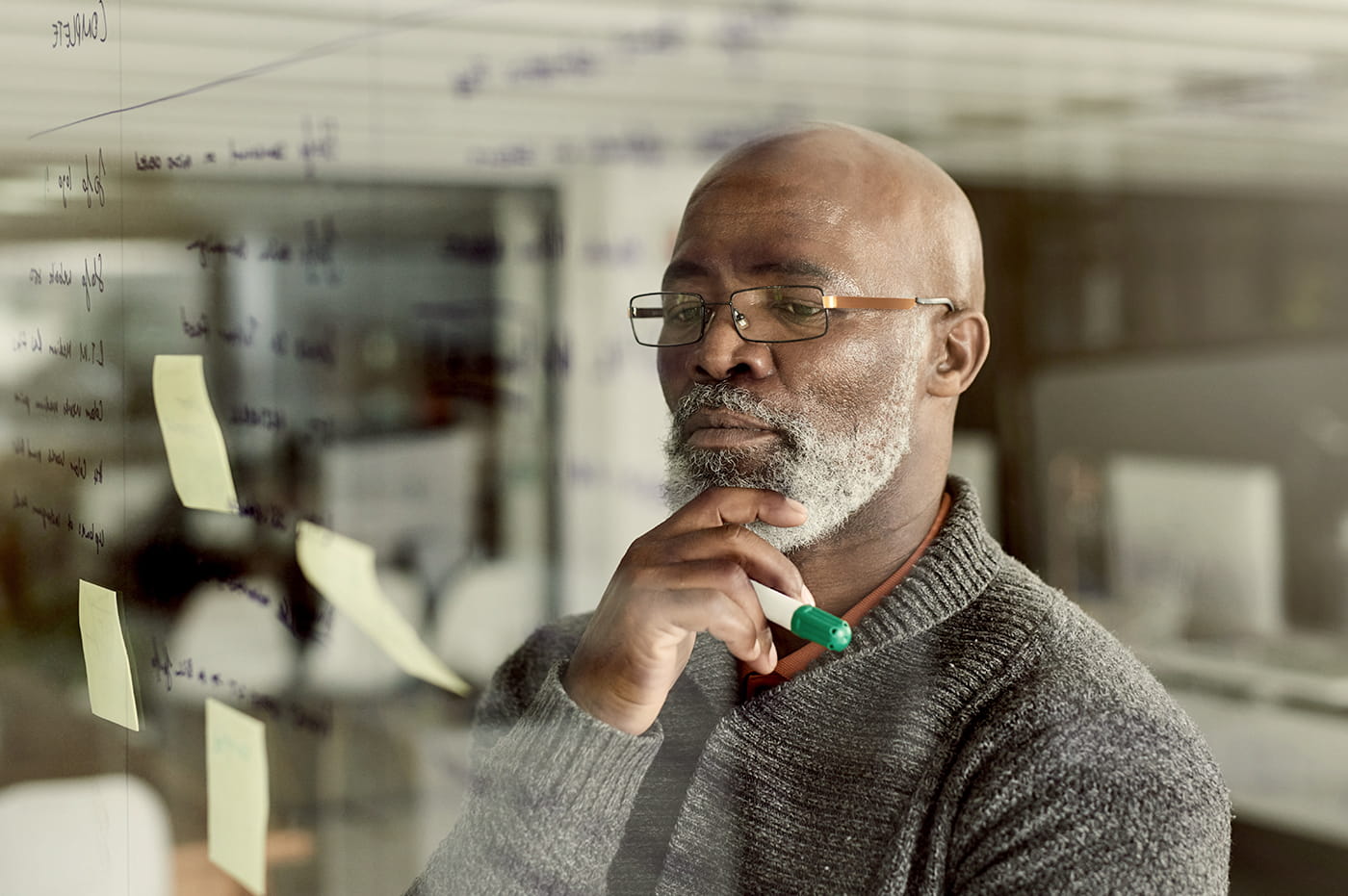 An older man looking at some sticky notes on a clear dry-erase board.