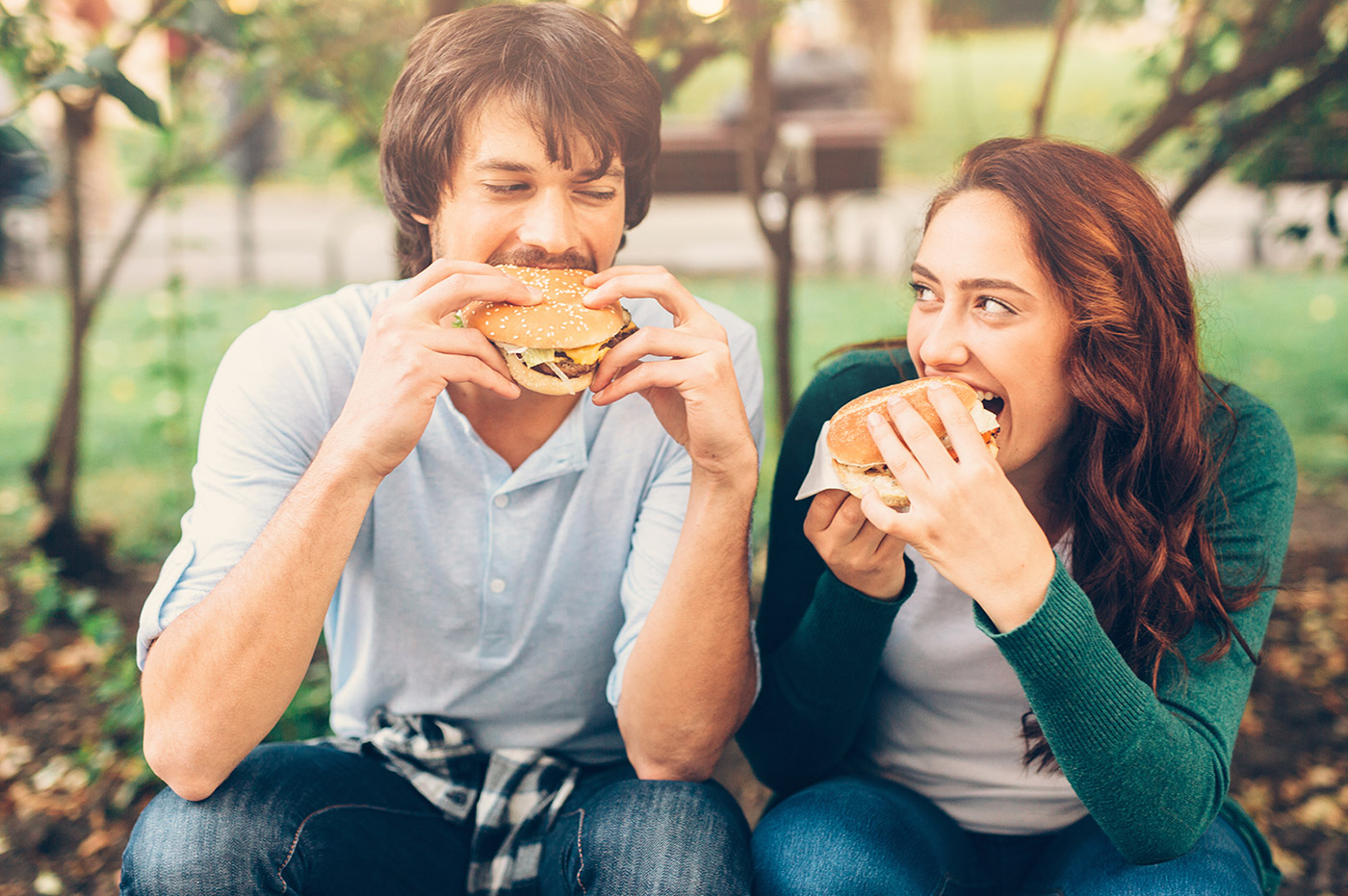 Man and woman in a park eating burgers