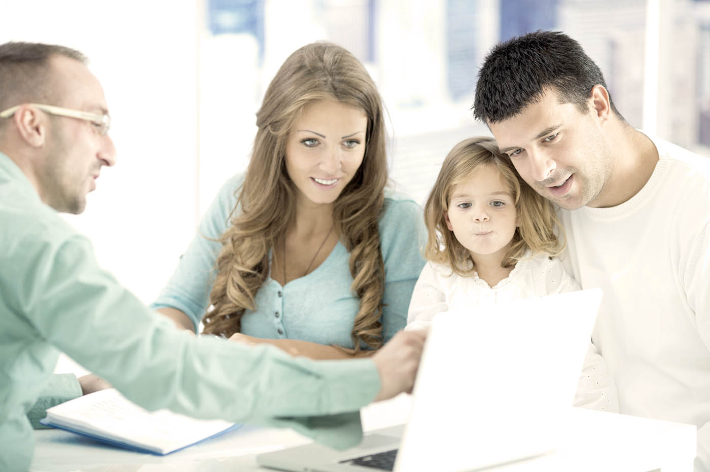 A young family looking at something a business person is pointing to on a laptop.