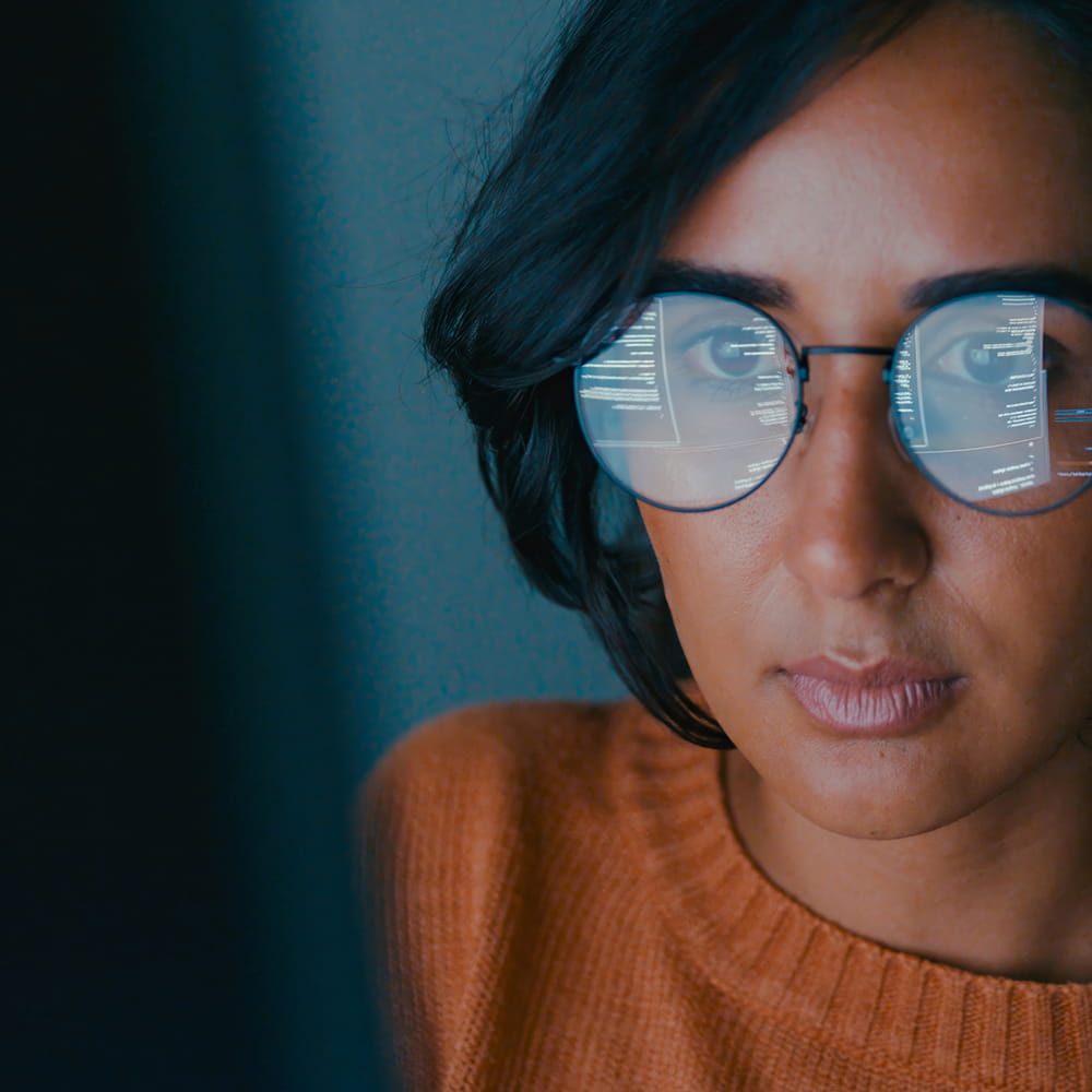 Woman looking at a computer screen with the code in her glasses reflection