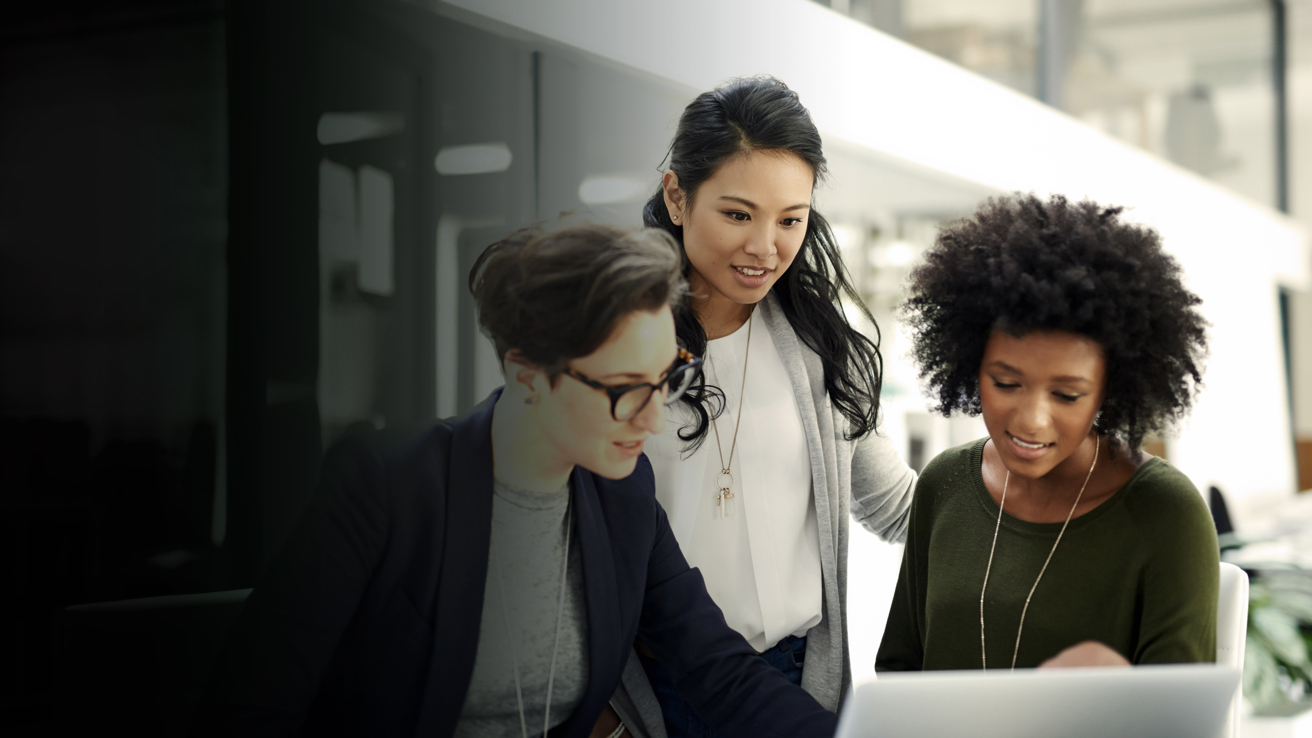 Three women gathered looking at a computer screen with a gradient overlay.