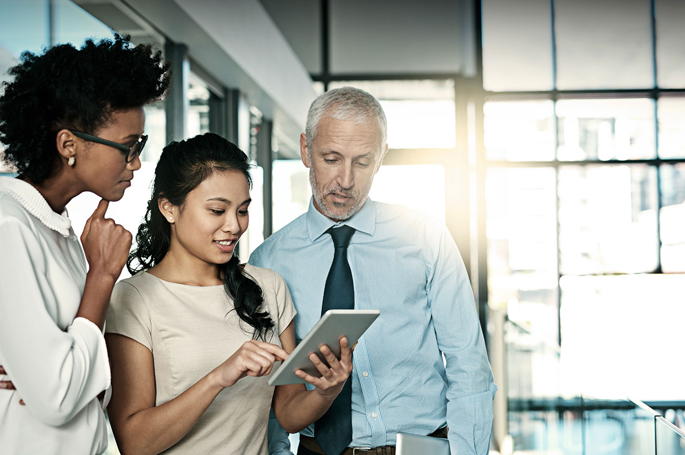 Three colleagues working on a tablet together.