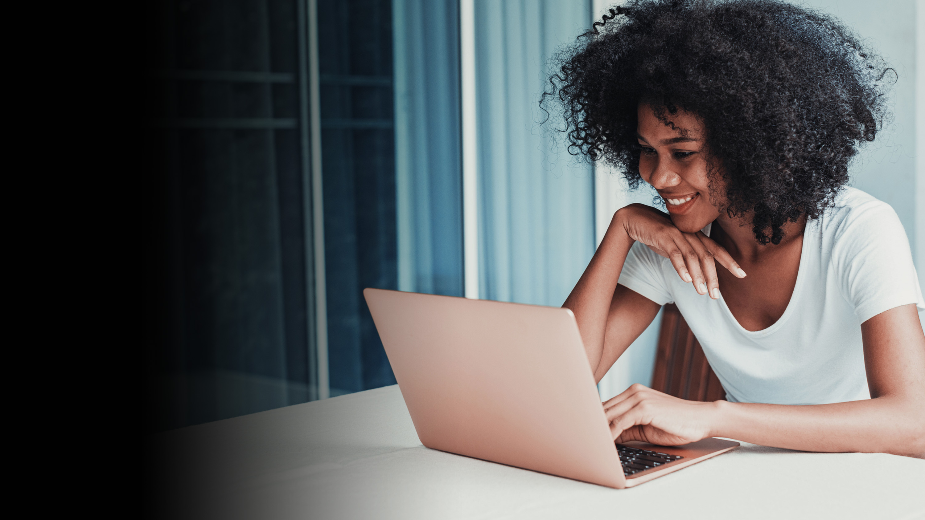 A woman working on a laptop on a balcony and smiling.