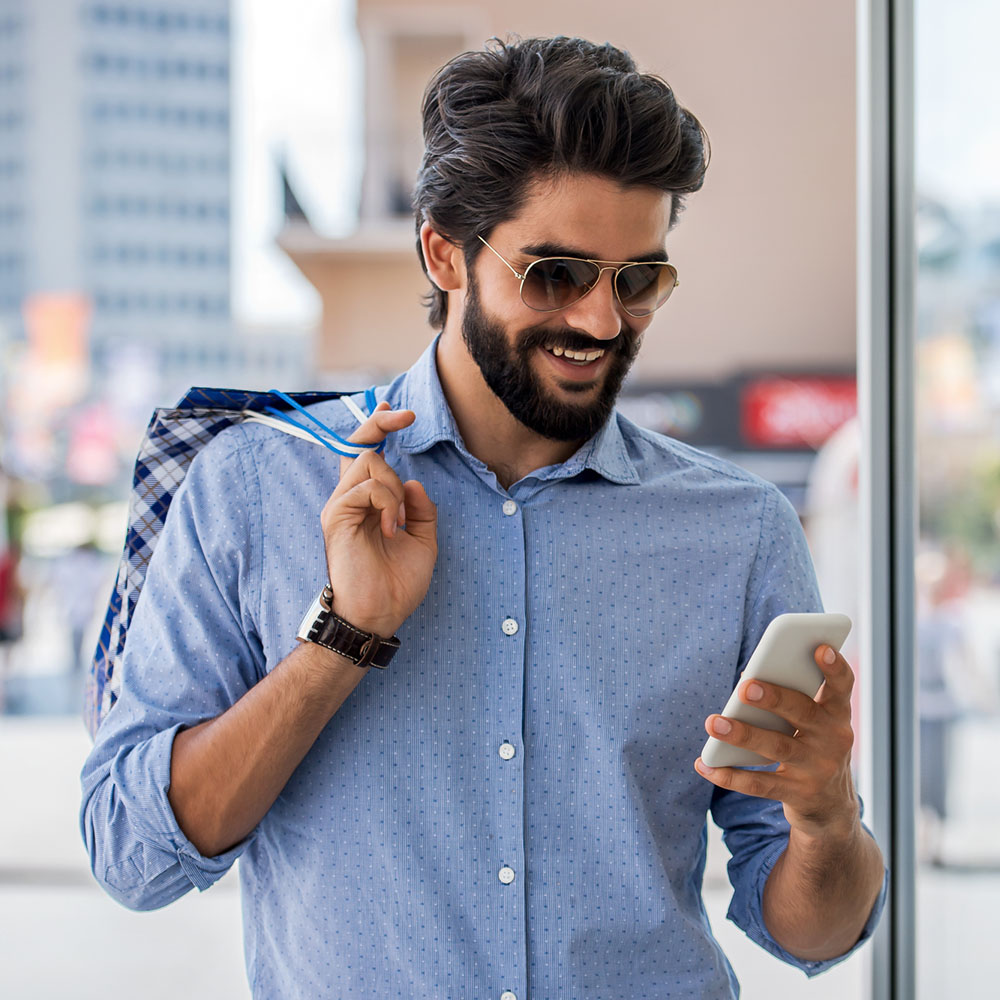  man in sunglasses looking at a smartphone and smiling.